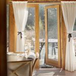 Holzgetäfeltes Interieur mit Glastüren zum Balkon. Weiße Vorhänge und hölzerner Stuhl.