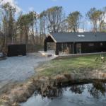 Modern cabin with terrace, garden, and small pond in the woods
