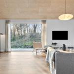 Living room with fireplace, large window, and sofa. Wooden ceiling and light walls.
