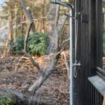 Outdoor shower at modern wooden cabin with forest in background.