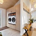 Washroom with integrated washing machines and wooden shelves. View of the forest through the door.