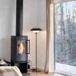 Wood-burning stove, large window with forest view, floor lamp, and curtains.
