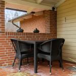 Terrasse mit Tisch und zwei Stühlen, rote Ziegelwand und Holzverkleidung.