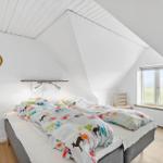 Bedroom with sloped ceiling, bed, window, and two chairs.