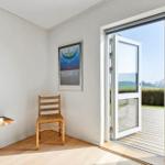 Room with chair, table, and poster on wall. Through glass door, terrace and landscape are visible.