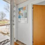 Entrance area with door and poster on the wall. Through the glass door, an outdoor area with a chair is visible.