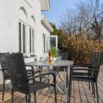 Deck with table and chairs, wooden floor, white house wall, trees in background.