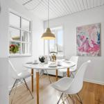 Dining room with round table, white chairs, and wooden floor. A painting hangs on the wall.