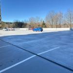 Großes Parkplatzareal mit mehreren Autos und Wohngebäude im Hintergrund.