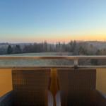 Zwei Stühle auf Balkon mit Blick auf Wald und Hügel bei Sonnenuntergang.