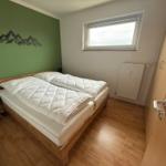 Schlafzimmer mit Doppelbett, grüner Wand und Fenster.