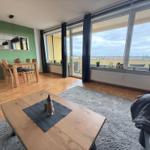 Wohn- und Essbereich mit Balkon, Holzboden und grüner Wand.