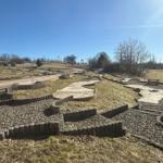 Ein Minigolfplatz mit Grasflächen und Kiesbereichen unter blauem Himmel.