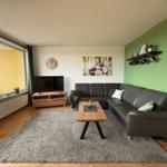 Wohnzimmer mit Sofa, Fernseher und großem Fenster.