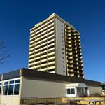 Hochhaus mit Balkonen und kleinem Nebengebäude unter blauem Himmel.