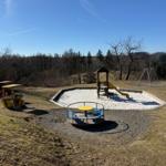 Kinder-Spielplatz mit Rutsche, Schaukel und Drehplattform auf grünem Grund.