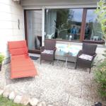 Terrasse mit Liegestuhl, zwei Stühlen und Tisch. Grünflächen und Steine umgeben den Platz.