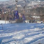 Schneebedeckter Hang mit Seilbahn und Blick auf das Dorf.