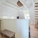 Dachgeschosszimmer mit Holztreppe und Stuhl. Deckenbalken und Fenster sichtbar.