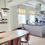 Essbereich mit Holztisch und Küchenbereich mit Insel und Fenstern.