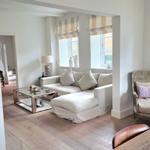 Wohnbereich mit Sofa, Sessel und Esstisch. Durchgang zur Treppe und Fenster mit Rollläden.