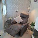 Ein braunes Relaxsessel mit Kissen, zwei runde Tische und eine Stehlampe.