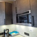 Küche mit dunklen Schränken und integriertem Backofen. Auf Arbeitsplatte stehen Kaffeemaschine und Tablett.