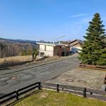 Haus mit Holzfassade, Straße und Blick auf bewaldete Hügel.