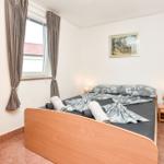 Schlafzimmer mit Bett, Nachttisch und Fenster mit Vorhängen.