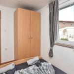 Schlafzimmer mit Bett, Kleiderschrank und Fenster mit Vorhängen.