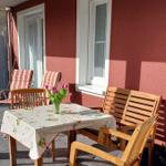 Terrasse mit Holztisch, Stühlen und Blumen. Rote Wand und Fenster.
