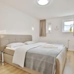 Schlafzimmer mit Doppelbett, Fenster, TV und Nachttisch.