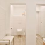 Bad mit Toilette, Dusche und Waschtisch. Fliesenwand und Holzboden.