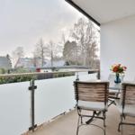 Terrasse mit Tisch, Stühlen und Blumenarrangement. Blick auf Bäume und Häuser.