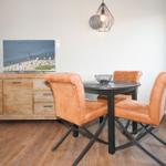 Esszimmer mit runden Tisch, drei orangefarbenen Stühlen und Holzsideboard.