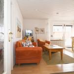 Wohn- und Essbereich mit orangefarbenem Sofa, Holztisch und Fenster.