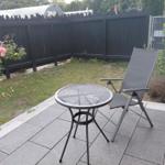 Terrasse mit Tisch und Stuhl, umgeben von Gras und Rosen.