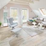 Wohnzimmer mit Sofa, Sessel und Fenstern. Holzboden und Dachschrägen.