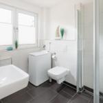 Badezimmer mit Dusche, Toilette, Waschmaschine und Fenster