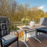 Terrasse mit Tisch und zwei Stühlen, Blick auf Wald und Himmel.
