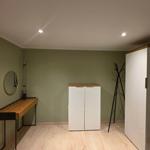 Ein Zimmer mit Holzboden, grünen Wänden, Schreibtisch, Kleiderständer und Schrank.