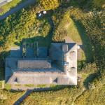 Haus mit Dach aus Stroh, umgeben von Grünflächen und einem Weg.