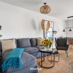 Ein Wohn- und Essbereich mit grauem Sofa, Holzboden und moderner Beleuchtung.