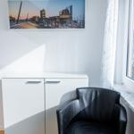 Schwarzer Sessel neben Fenster mit Gardine. Weiße Schrankwand und Wandbild.