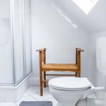 Badezimmer mit Toilette, Dusche und Holzstuhl.