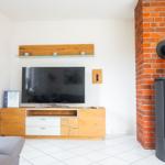 Wohnzimmer mit Fernseher, Holzmöbel und Kaminofen an Backsteinwand.