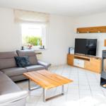 Wohnzimmer mit Sofa, TV und Kaminofen an Backsteinwand.