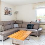 Ein Wohnzimmer mit braunem Sofa, Holztisch und Fenster mit Blick nach draußen.