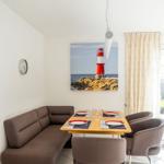 Esszimmer mit braunem Sofa, Tisch und Stühlen. Wandbild zeigt Leuchtturm.