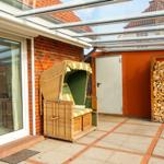 Terrasse mit Rattanliege, Holzstapel und Glasdach. Zugang über Schiebetür.